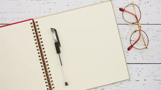Beyaz ahşap masada açık defter, kalem ve gözlük